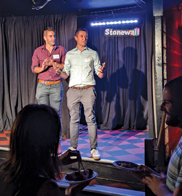 Two men address an audience on what looks like a small stage with "Stonewall" visible in the background